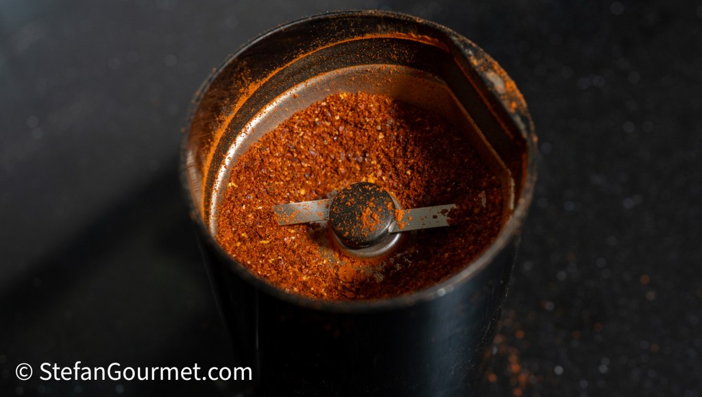 Grinding dried chiles in a spice grinder, showing a close-up of the spice mix inside.