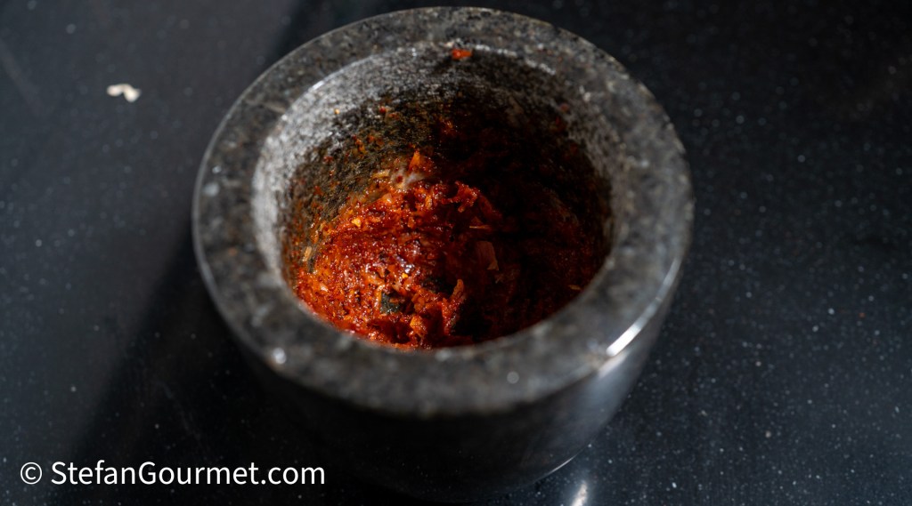 A close-up of a mortar filled with red chili paste, placed on a dark countertop.