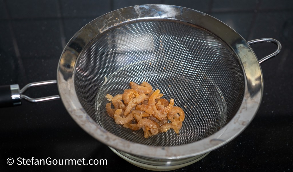 A strainer containing soaked dried shrimp inside a kitchen setting.