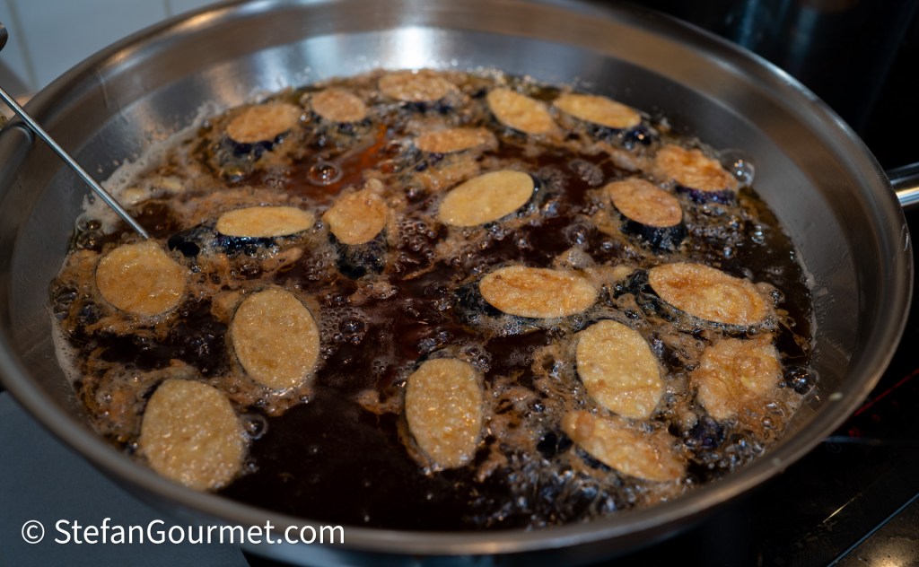 Slices of Thai eggplant frying in hot oil until golden brown.