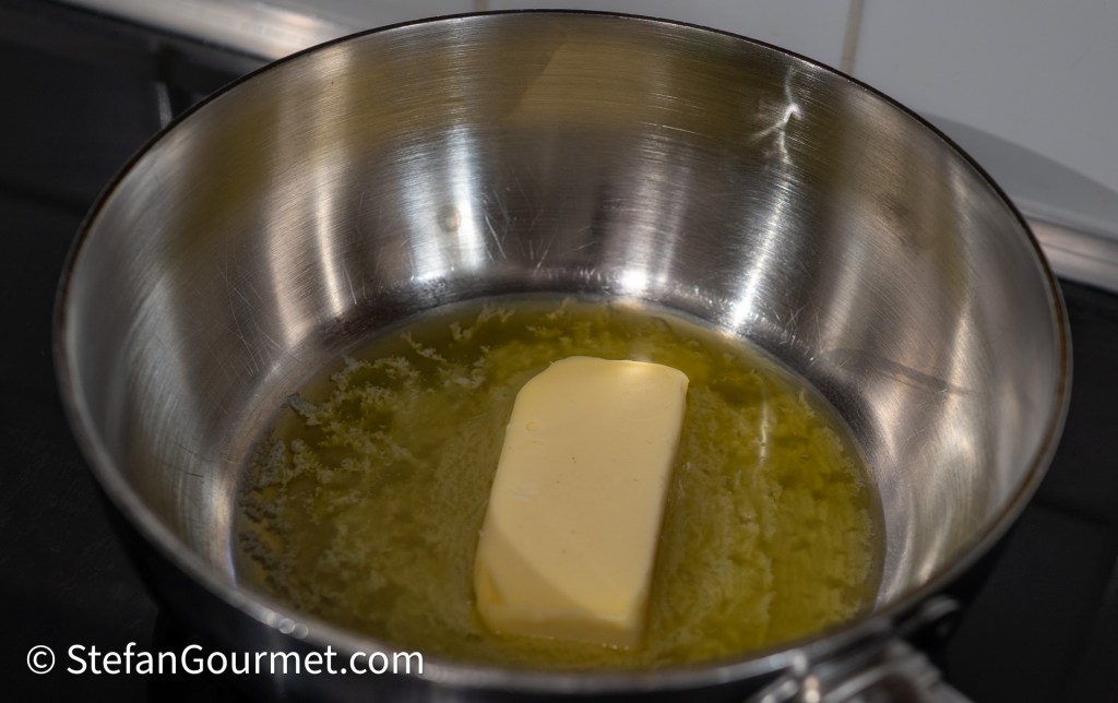 A stick of butter melting in a stainless steel saucepan on a stovetop.