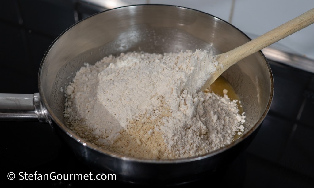 A pan with a mixture of almond meal and flour being stirred with a wooden spoon.