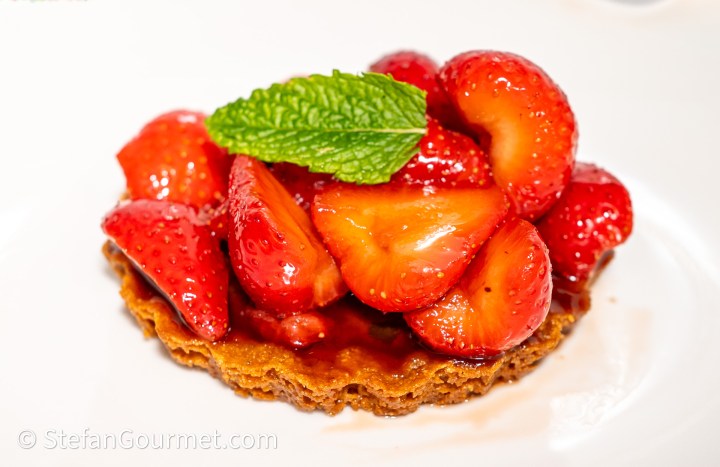 A crisp almond shell filled with fresh macerated strawberries, topped with a sprig of mint.