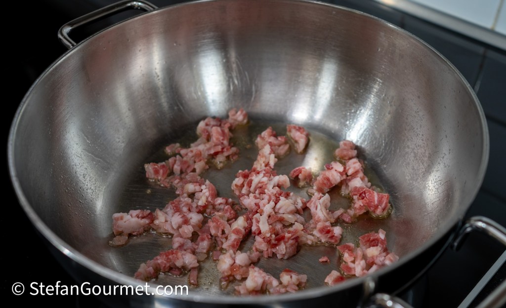 Finely minced pancetta cooking in a stainless steel pan with a small amount of oil.