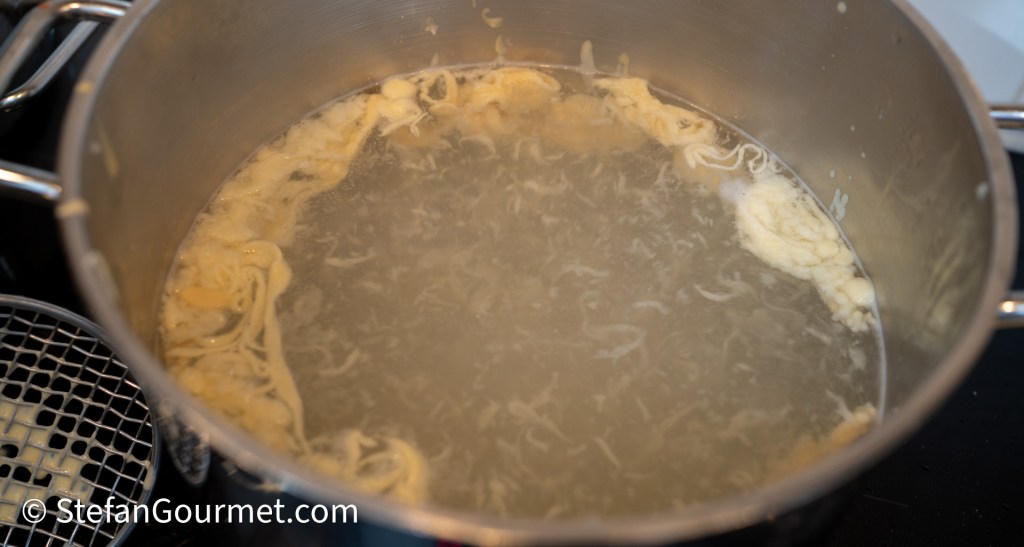 Fresh pasta droplets cooking in boiling water in a pot.