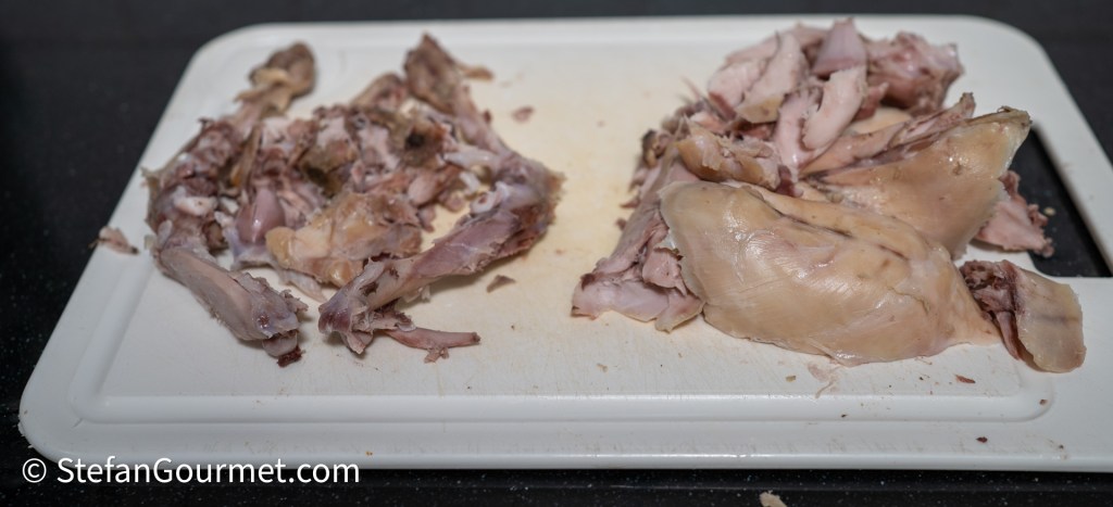 Chopped rabbit meat on a cutting board, separating the bones and tender pieces ready for cooking.
