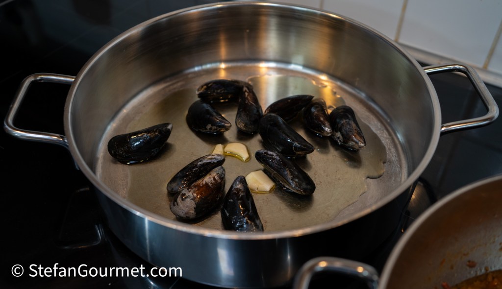 A pot with mussels and garlic in olive oil, ready for cooking on a stovetop.