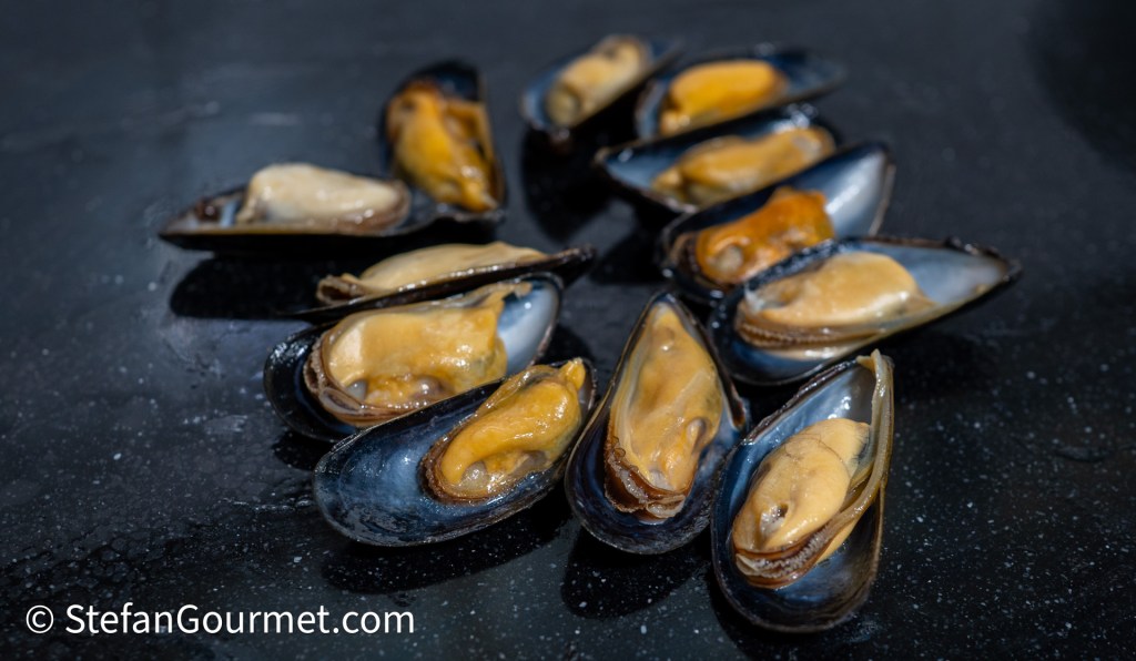 Fresh mussels in their half shells arranged on a dark surface.