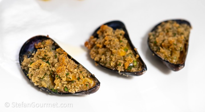 Three gratinated mussels topped with a golden breadcrumb mixture, served on a white plate.
