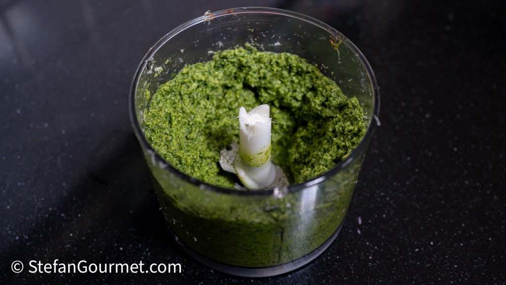 A close-up view of freshly blended green pesto in a food processor, showcasing its vibrant color and texture.
