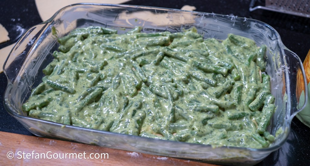 A baking dish filled with green beans mixed with pesto and béchamel sauce, ready for the oven.