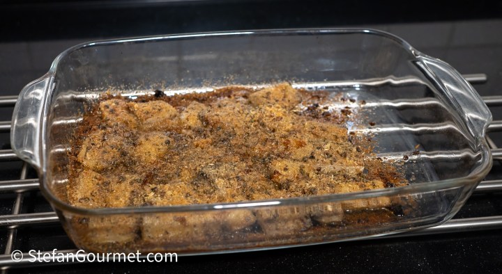 A glass baking dish containing a baked dish with a golden-brown crust, resting on a black surface.
