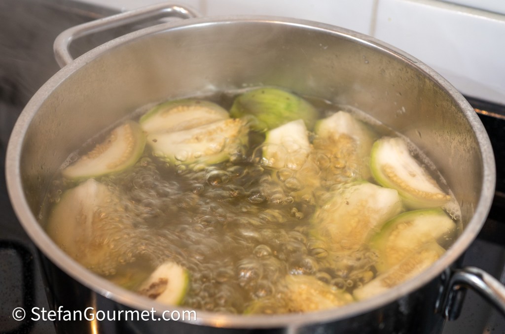 A pot of boiling water with slices of green and white fruit submerged, creating bubbles.