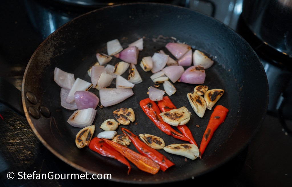A frying pan containing sautéed shallots and sliced red chili peppers, some pieces showing a browned texture from cooking.