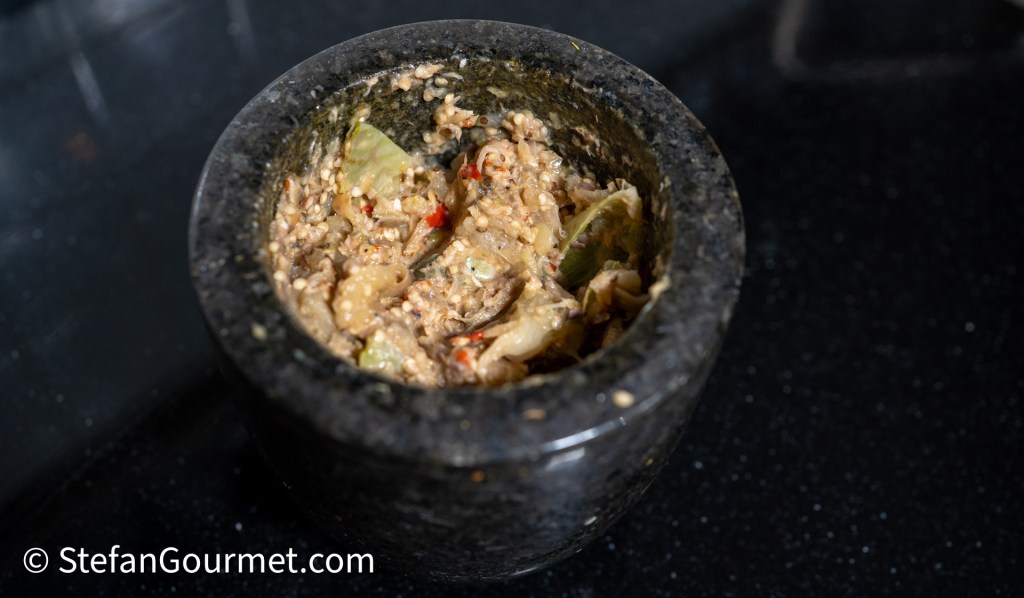 A stone mortar containing a mixture of ground ingredients, including sesame seeds and various spices, on a dark countertop.