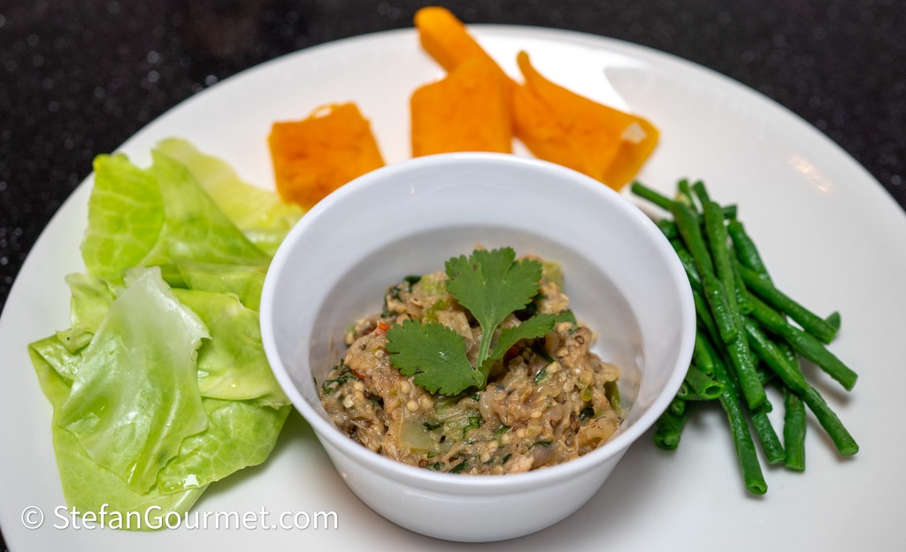 A plate featuring a bowl of savory dip garnished with fresh cilantro, surrounded by green lettuce leaves, cooked green beans, and chunks of orange squash.