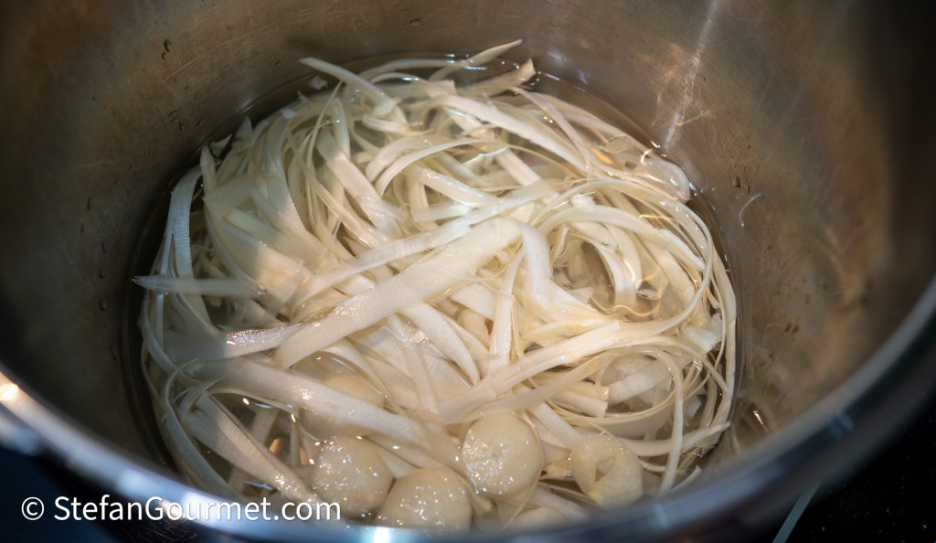 Thinly sliced ingredients submerged in water inside a pot.