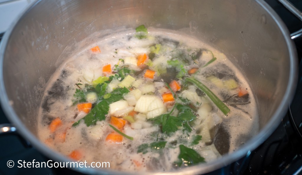 A pot of simmering vegetable broth with chopped carrots, celery, onions, and fresh herbs.