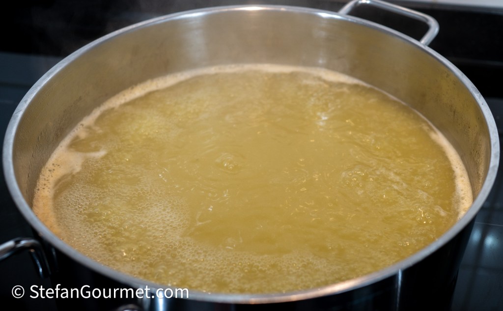 A large pot filled with boiling water on a stovetop, producing steam and bubbles.