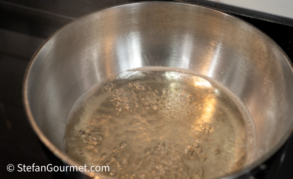 A stainless steel pot filled with bubbling water on a stovetop.