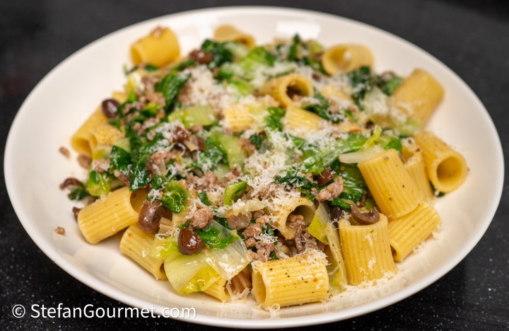 A plate of rigatoni pasta topped with sautéed greens, ground meat, and grated cheese.