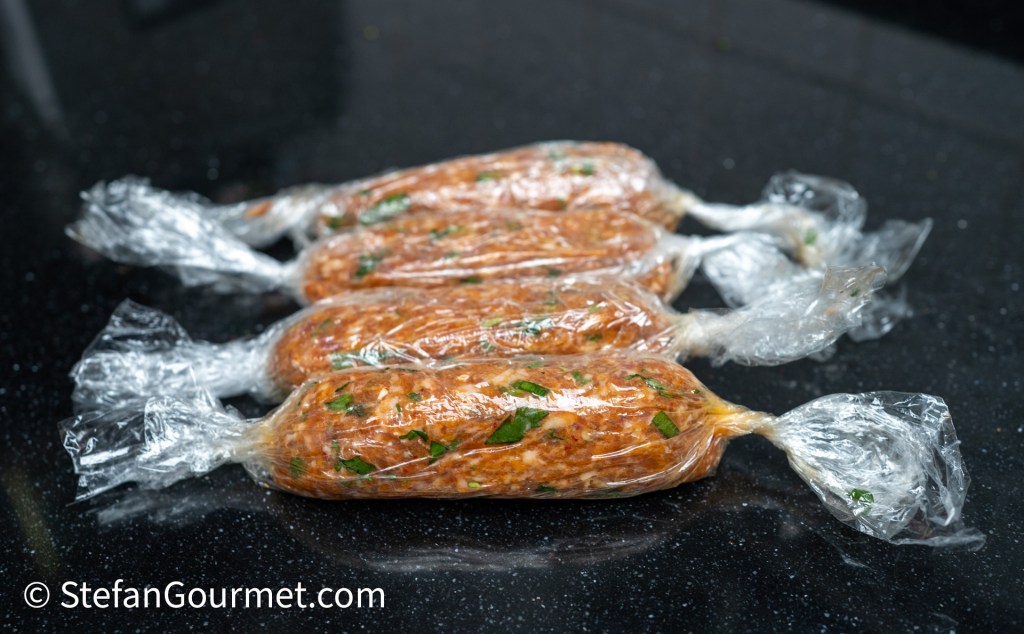Four sausage-shaped food items wrapped in clear plastic, placed on a dark countertop.