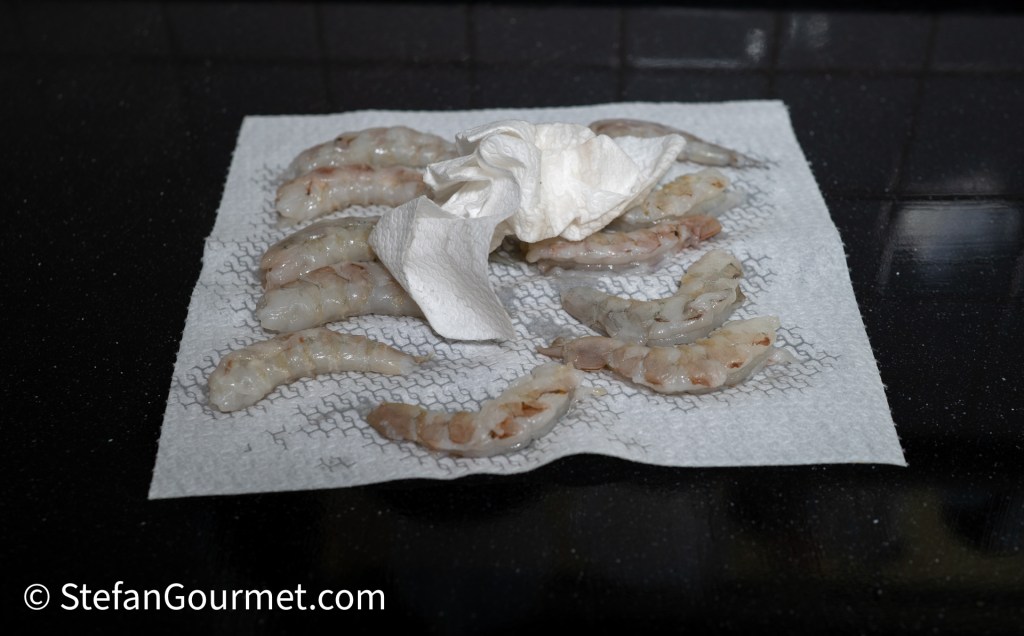 Raw shrimp on a paper towel, with a crumpled paper towel nearby, set against a black countertop.