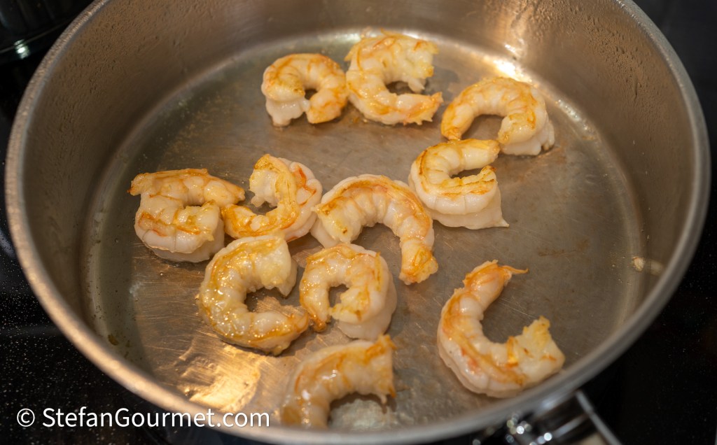 Pan-seared shrimp cooking in a stainless steel skillet.