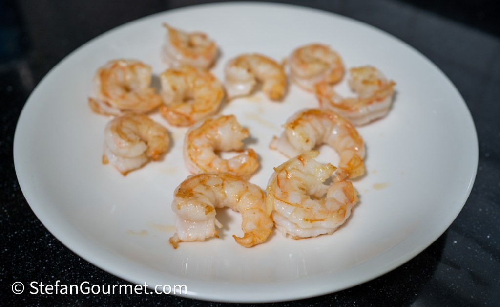 A plate of cooked shrimp arranged in a circular pattern on a white dish.