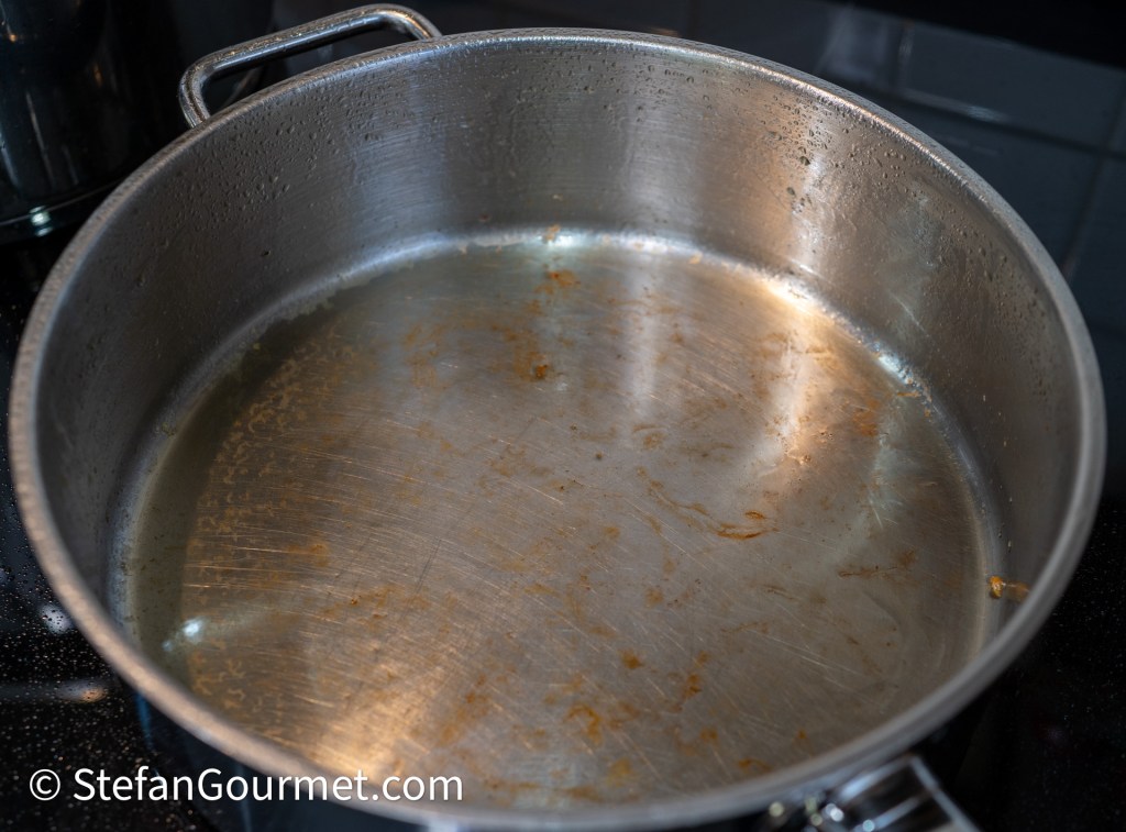 A large, empty stainless steel pot with slight residue at the bottom, sitting on a stovetop.