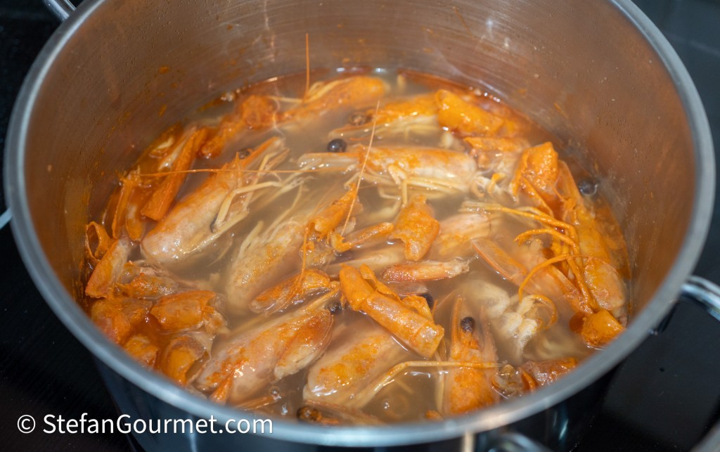 A pot filled with boiling water and cooked crustaceans, including shrimp and their shells, in a rich, reddish broth.