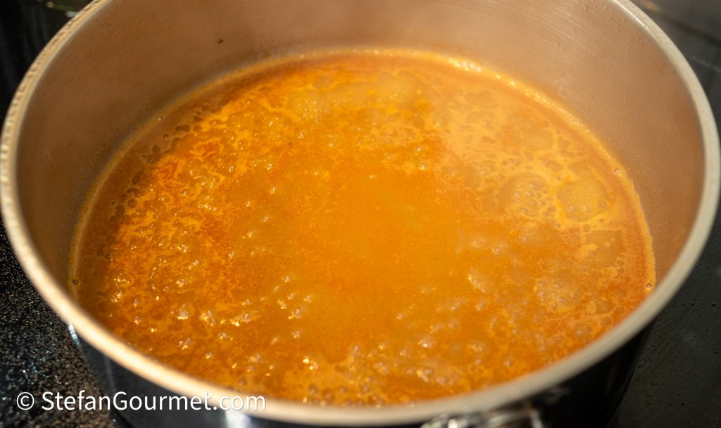 A close-up of simmering soup or sauce in a stainless steel pot, with bubbles and steam rising.