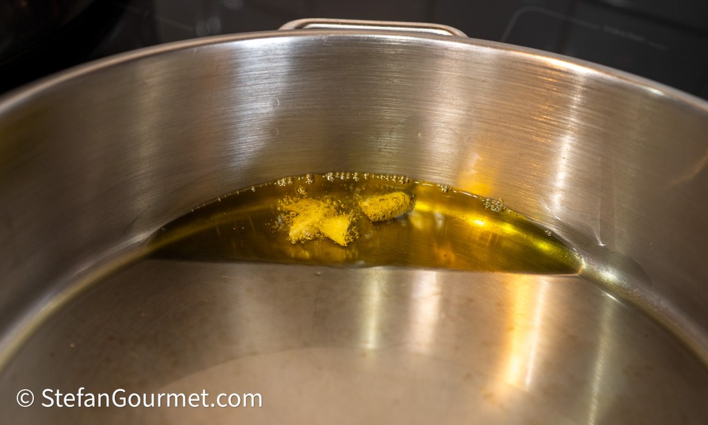 A close-up of a stainless steel pot with a small piece of butter melting in olive oil, producing bubbles.