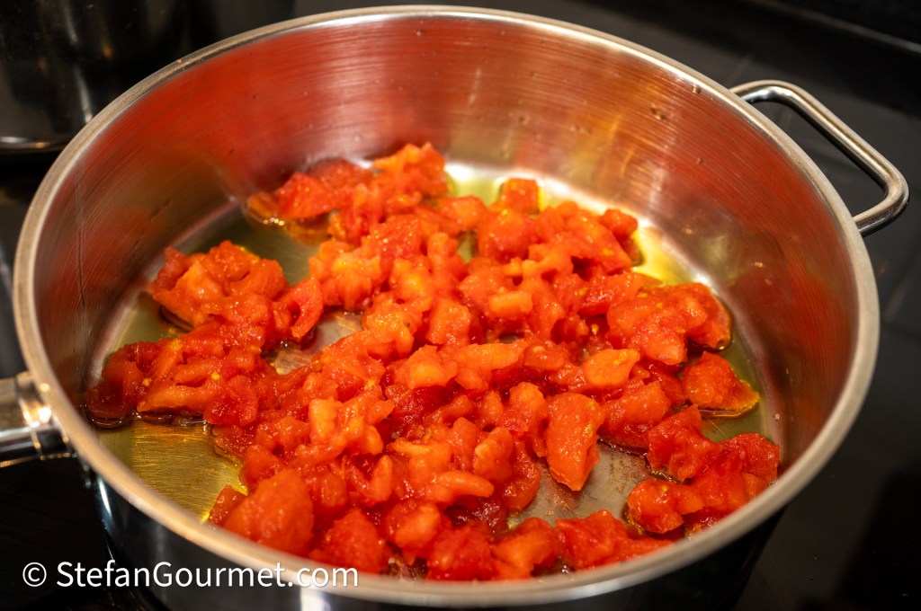 Chopped tomatoes cooking in a stainless steel pan on a stovetop.