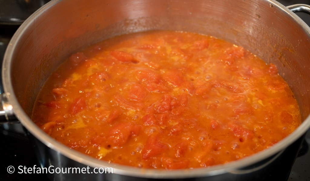 A pot of simmering tomato sauce with visible chunks of tomatoes, bubbling on a stovetop.