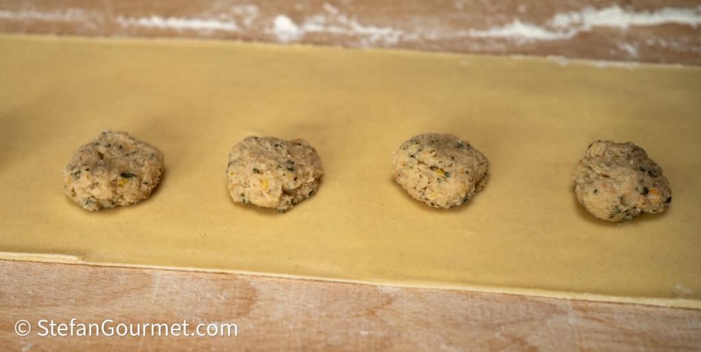 Four dough balls placed on a sheet of rolled pasta dough, prepared for making filled pasta.