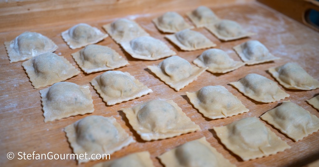 Freshly made ravioli arranged on a wooden surface, lightly dusted with flour.