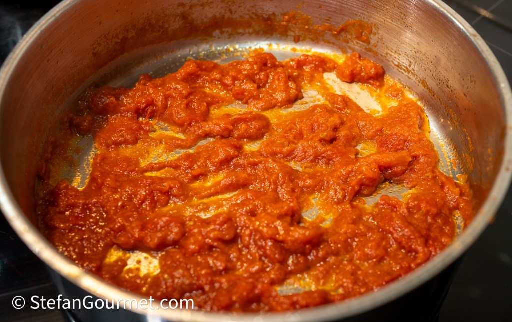 A close-up view of a metallic pot containing a thick, rich red sauce with some visible texture, indicating it's been simmered or reduced.