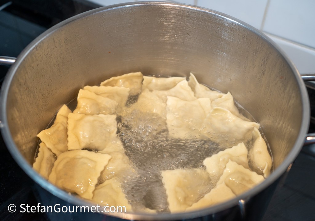 A pot of boiling water with several ravioli cooking inside.