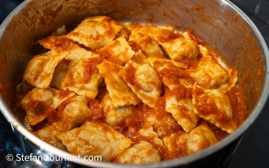 A pot filled with ravioli smothered in tomato sauce, showcasing the pasta's texture and rich red sauce.