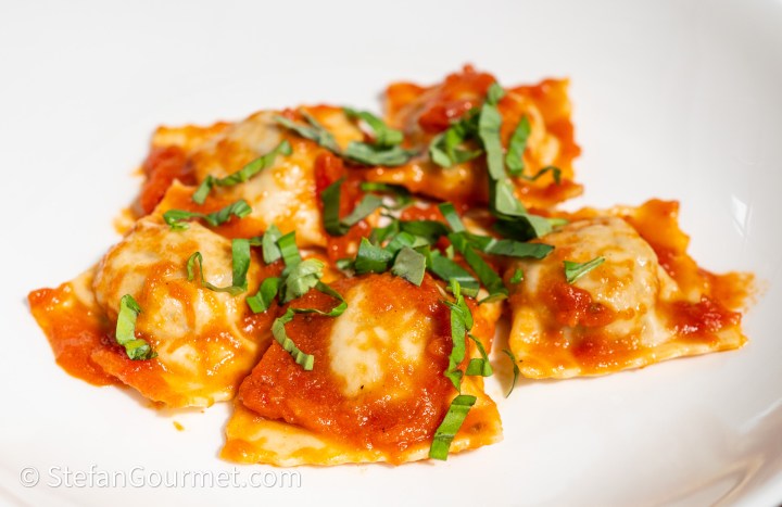 A plate of ravioli topped with marinara sauce and garnished with fresh basil.