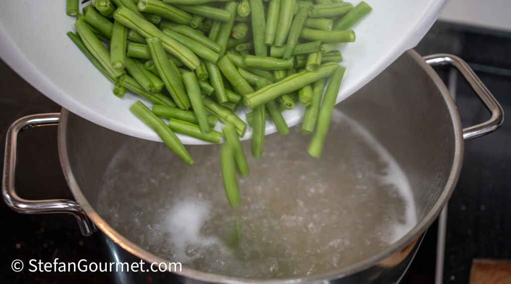 Fresh green beans being poured into a pot of boiling water.