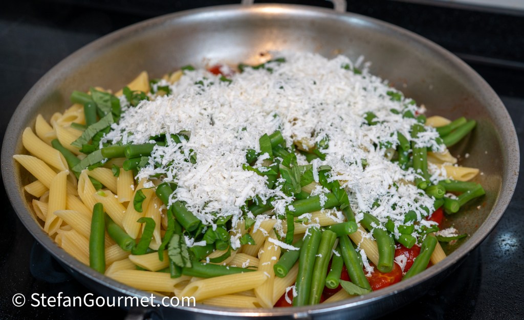A skillet filled with pasta, topped with green beans, fresh herbs, and shredded cheese.