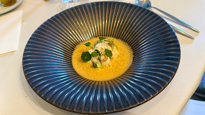 A beautifully plated dish featuring creamy soup with delicate garnishes, served in a deep, textured bowl.