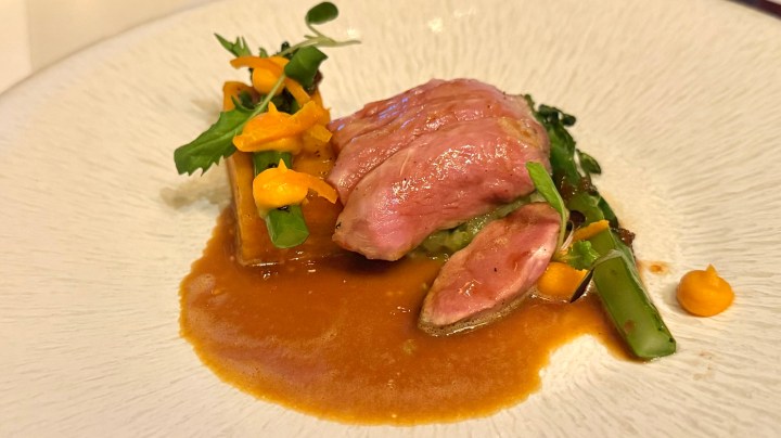 A plate featuring a serving of cooked meat with a slice cut, accompanied by vegetables and a savory sauce.