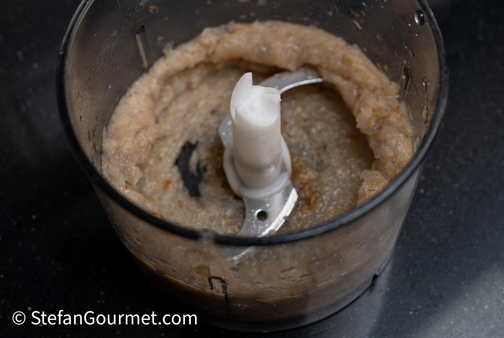 Close-up of a food processor with blended ingredients inside, showing a creamy mixture around the blades.