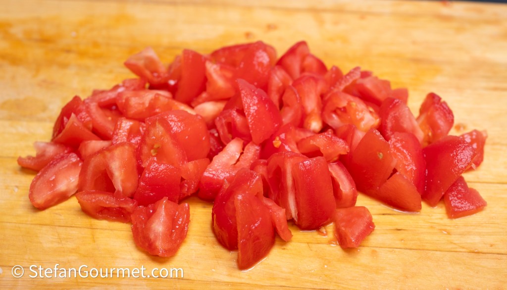 Chopped red tomatoes on a wooden cutting board.